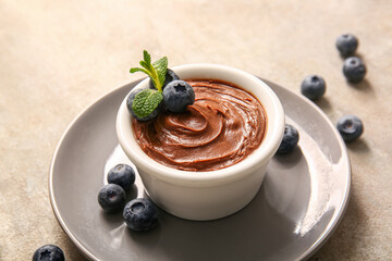 Plate with bowl of delicious chocolate pudding and blueberry on grey table