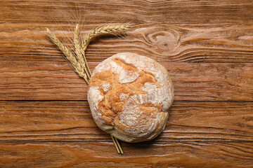 Loaf of fresh bread with wheat ears on wooden background