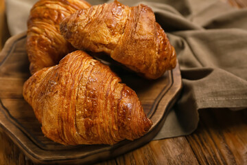 Board with delicious croissants on wooden background, closeup