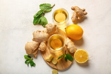 Wooden board with cups of tea, lemon, ginger and mint on light background