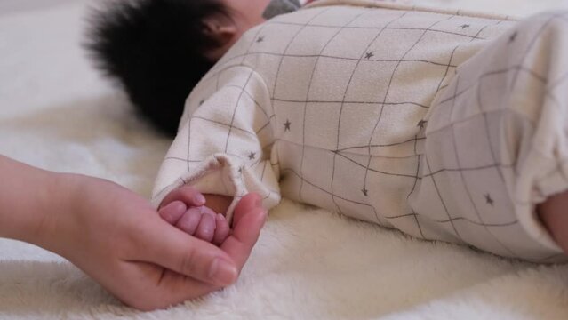 乳児の赤ちゃんの手を大人の手が下からすくう動画