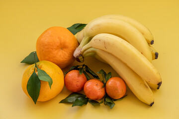 Bananas, oranges and tangerines on a yellow background. Healthy food isolated on yellow