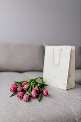 A bouquet of pink fresh tulips lies on a beige fabric and a white gift bag. Valentine's Day background
