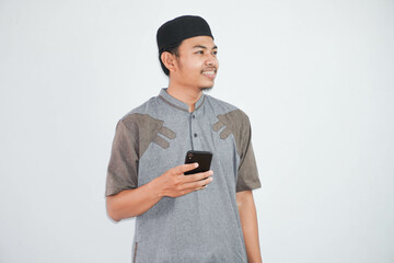 Happy or smiling young asian muslim man holding phone cellular wearing koko clothes isolated on white background. Ramadan concept