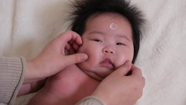 乳児の赤ちゃんが保湿剤を顔に塗られている様子の動画