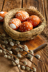 Board with nest of Easter eggs and willow branches on wooden background, closeup