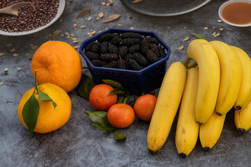A few oranges, tangerines, mulberries in the box and a ripe banana on a kitchen table