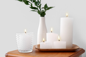 Burning candles and vase with ruscus branches on end table near grey wall