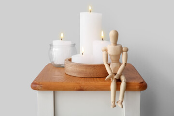 Burning candles and wooden mannequin on end table near grey wall