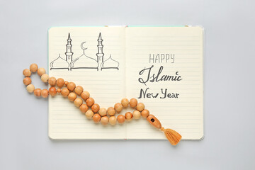 Notebook with text HAPPY ISLAMIC NEW YEAR and prayer beads on light background