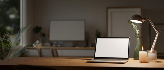 Minimal workspace with laptop mockup, candles, table lamp, and copy space on wood table