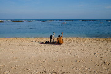 A Parent sitting on the sand beach and waving their hands to the kids on the sea at Pandawa Beach, Bali, Indonesia