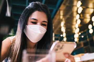 A woman wearing a mask holding a phone and read something on her phone in the restaurant