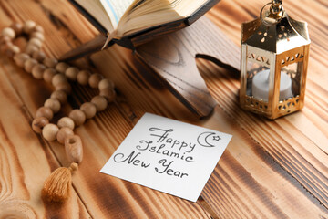 Card with text HAPPY ISLAMIC NEW YEAR, lantern, Koran and prayer beads on wooden background, closeup