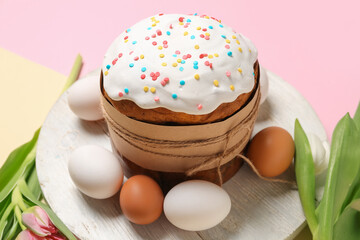 Board with Easter cake, eggs and tulip flowers on pink and beige background