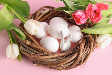 Nest with Easter eggs, bunny and tulip flower on pink background