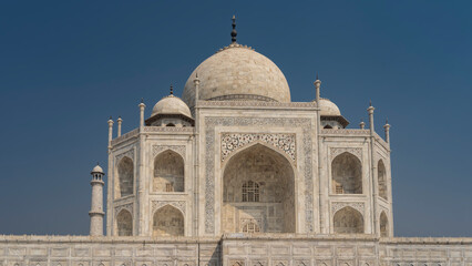 Obraz premium The beautiful ancient mausoleum of the Taj Mahal against the blue sky. Symmetrical white marble building with domes and minarets. Carvings and inlays of precious stones are visible on the walls. India