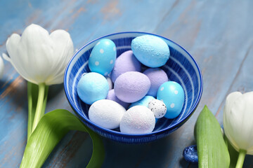 Bowl of painted Easter eggs and tulip flowers on color wooden background, closeup