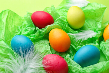 Fototapeta na wymiar Painted Easter eggs and feathers on color crumpled paper, closeup