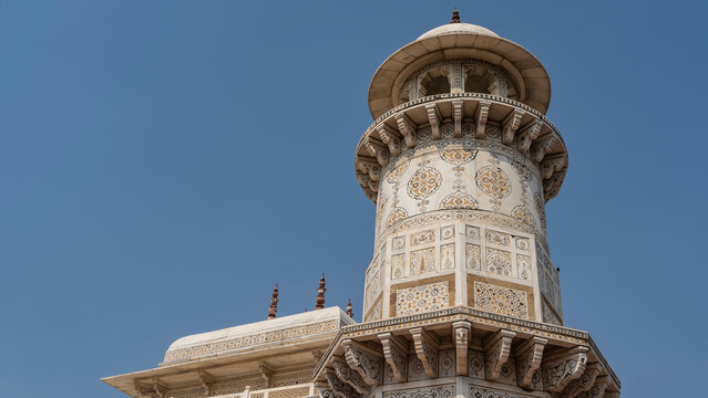 The ancient mausoleum -the grave of Itmad-Ud-Daul. Marble minaret against the blue sky. Balconies, spires are visible. There are ornaments and inlays of precious stones on the walls. India. Agra