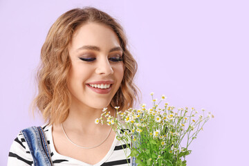 Beautiful happy young woman with bouquet of chamomiles on lilac background