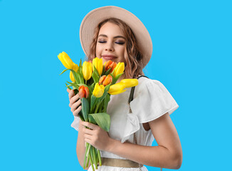 Beautiful happy young woman with bouquet of tulips on light blue background