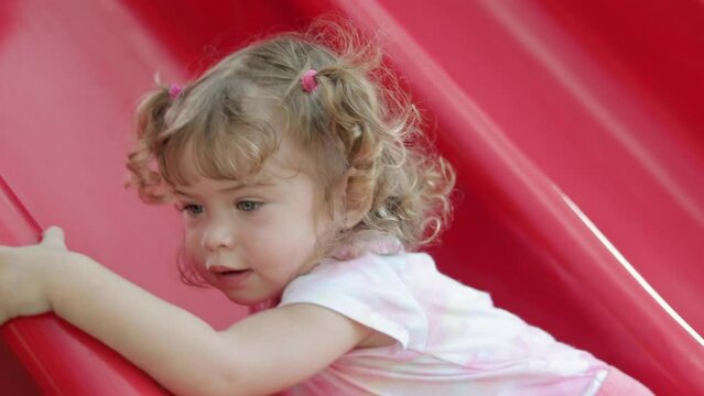 Beautiful little girl playing on a red slide at a playground