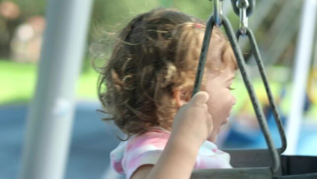 Mother pushing her ittle girl on a swing at playground