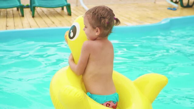 Side view of little girl jumping in swimming pool with yellow inflatable ring. Slow motion. 4k