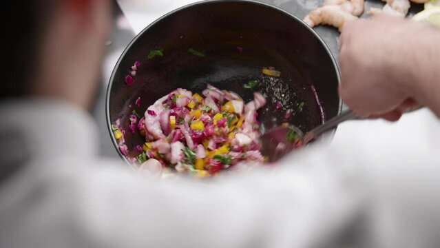 Chef prepares cebiche by spooning ingredients into bowl,