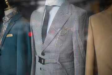 old fashioned men's suits through a shop window. Retro fashion with prince of wales check, creme colored jackets, shirts and ties. - obrazy, fototapety, plakaty