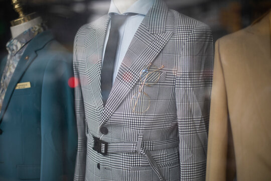 old fashioned men's suits through a shop window. Retro fashion with prince of wales check, creme colored jackets, shirts and ties.