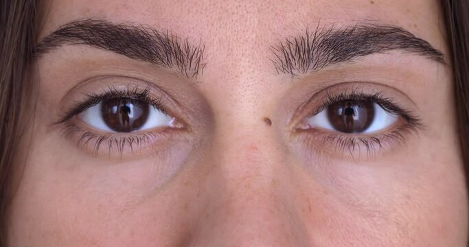 Close-up face of young woman opening her eyes. Close up portrait, two brown woman's eyes looking into the camera in slow motion.