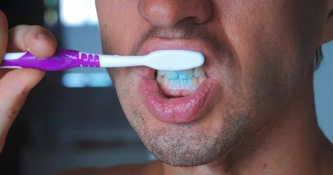 Extreme close up male brushing teeth with manual toothbrush in bathroom at home. Male 30s cleaning teeth with tooth brush and toothpaste at bath. Dental health concept, close up brushing teeth