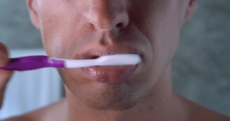 Close up male mouth, teeth brushing with manual toothbrush in bathroom at home. Young male cleaning teeth, dental health concept, close up brushing teeth