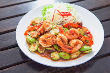 Fototapeta na wymiar Phad Sato, stir-fried prawns with curry paste (Thai food), white plate, placed on a wooden table