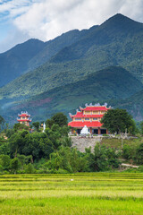 Distant view over rice fields of an ancient temple at the base of high mountains at Da Nang in Vietnam