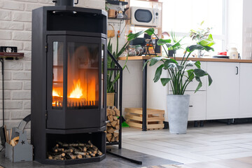Black Metal Steel fireplace stove with fire and firewood near kitchen in village house. Cozy home...
