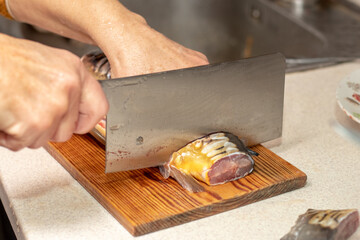 A woman cuts fish with a large knife at home in the kitchen