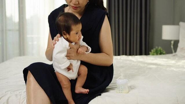 mother holding burping and crying baby in a bedroom after feeding milk
