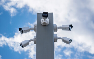 Several modern surveillance CCTV cameras in different directions, on wide metal pole against sky
