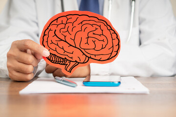 Doctor in a uniform holding a brain symbol made from red paper while sitting at the table