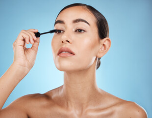 Fototapeta premium Mascara, application and woman with makeup on face isolated on a blue background in a studio. Beauty, glam and model with cosmetics from a brush on an eyelash for facial treatment on a backdrop