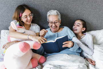 Hispanic family grandmother and granddaughter reading a book in bed at home in Latin America