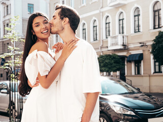 Fototapeta premium Smiling beautiful woman and her handsome boyfriend. Happy cheerful family. Sexy couple posing in the street at sunrise. During romantic date at sunny summer day outdoors. Looking at each other. Kiss