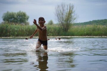 The boy runs out of the water. Portrait of a child merrily running from the water to the shore in splashes. Selective focus