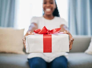 Christmas, gift and a box in the hands of a black woman in her home, sitting on the living room...