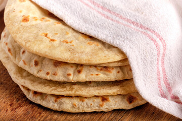Stack of freshly baked pita under a white towel