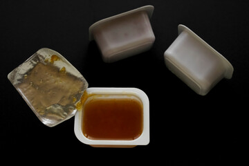 3 three peach fruit jam in white plastic boxes. isolated on black background. aluminum foil cover.
