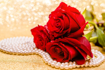 Red rose and pearl necklace on a shiny gold background
